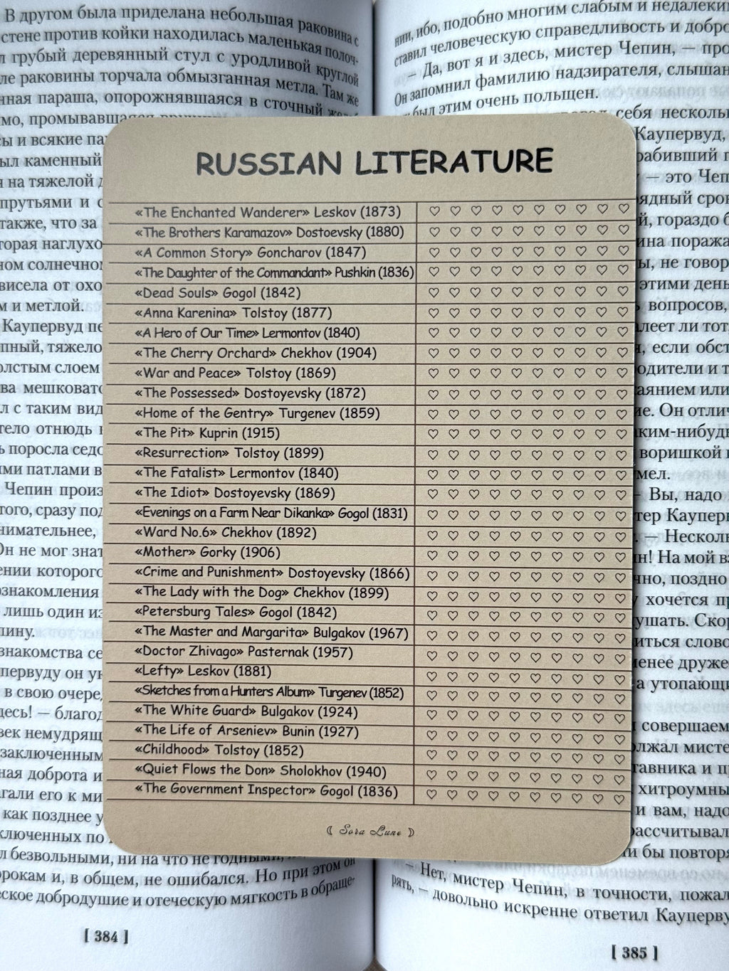 A rectangular educational poster titled 'RUSSIAN LITERATURE' with a list of Russian literary works and authors marked with small circles, placed on top of open books showing printed Cyrillic text.
