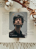 A rectangular bookplate featuring a portrait of Neil Gaiman lies on an open book, styled with dried flowers and a knitted cream blanket underneath.